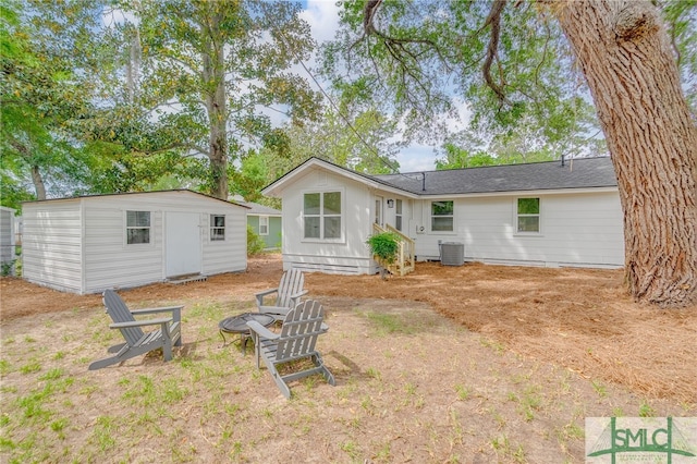 back of property featuring a fire pit, an outdoor structure, central AC, and a shed