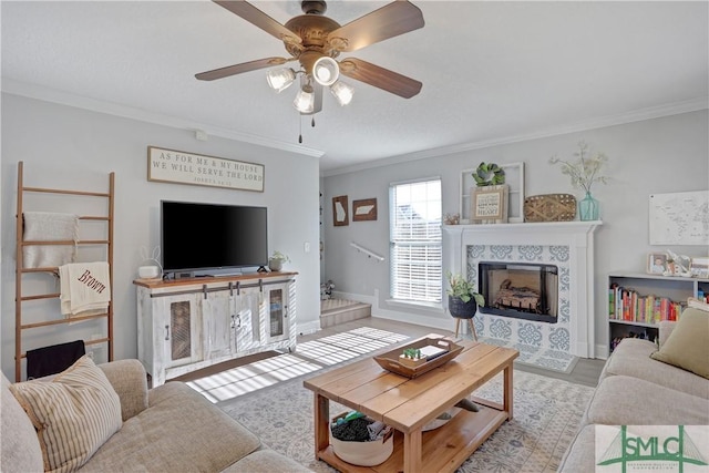 living area featuring a tiled fireplace, baseboards, a ceiling fan, and crown molding