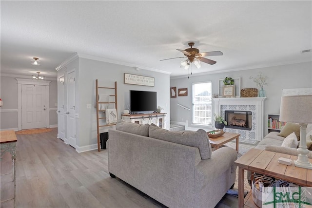 living room with light wood finished floors, a tiled fireplace, a ceiling fan, and ornamental molding