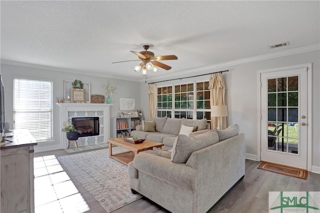 living room featuring wood finished floors, visible vents, a premium fireplace, crown molding, and ceiling fan