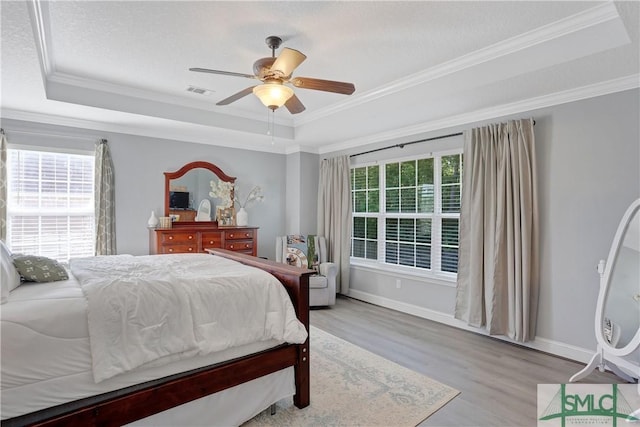 bedroom featuring ornamental molding, wood finished floors, and a tray ceiling