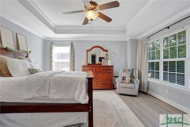 bedroom featuring ornamental molding, light wood finished floors, and a raised ceiling