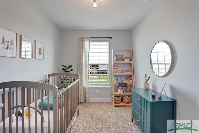 bedroom with baseboards, a textured ceiling, a crib, and light colored carpet