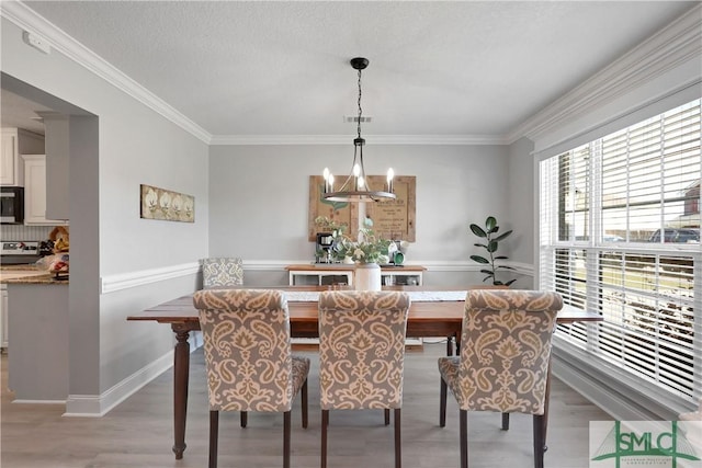 dining space featuring light wood-style floors, crown molding, and an inviting chandelier