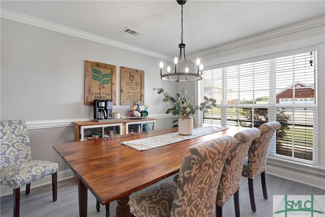 dining room with wood finished floors, an inviting chandelier, a healthy amount of sunlight, ornamental molding, and visible vents