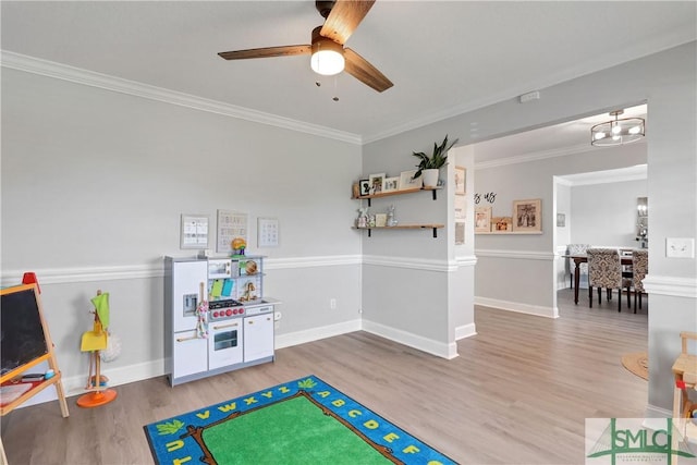 recreation room featuring baseboards, crown molding, light wood-style floors, and ceiling fan with notable chandelier
