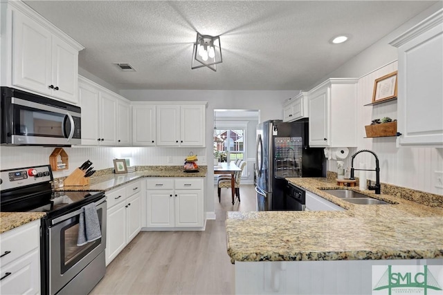 kitchen with light wood finished floors, visible vents, a sink, appliances with stainless steel finishes, and white cabinetry