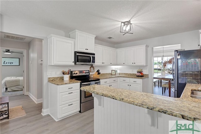 kitchen featuring white cabinets, a peninsula, visible vents, light stone countertops, and appliances with stainless steel finishes