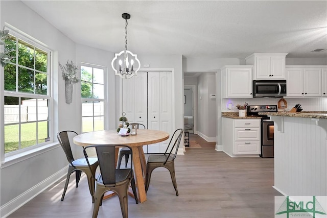 dining room featuring visible vents, light wood finished floors, baseboards, and an inviting chandelier
