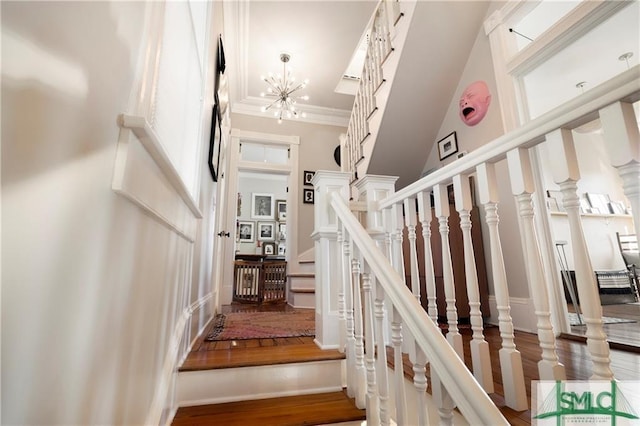 stairs featuring a chandelier, wood finished floors, a high ceiling, a decorative wall, and ornamental molding