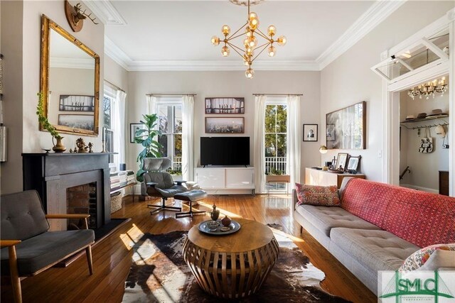 living room featuring a fireplace, a notable chandelier, ornamental molding, and wood-type flooring