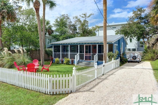 view of front of home featuring a fenced front yard, driveway, a sunroom, a front yard, and metal roof