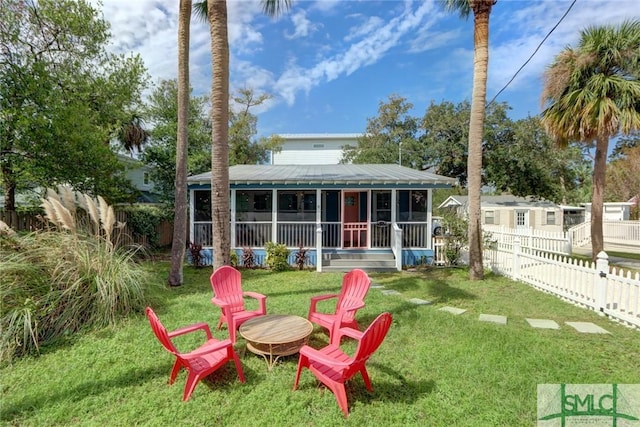 rear view of house with a fenced backyard, a yard, a fire pit, a sunroom, and metal roof