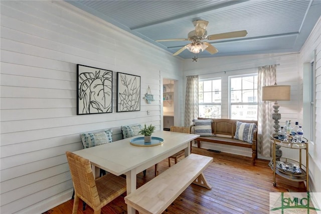 dining area with wooden walls, hardwood / wood-style floors, and a ceiling fan