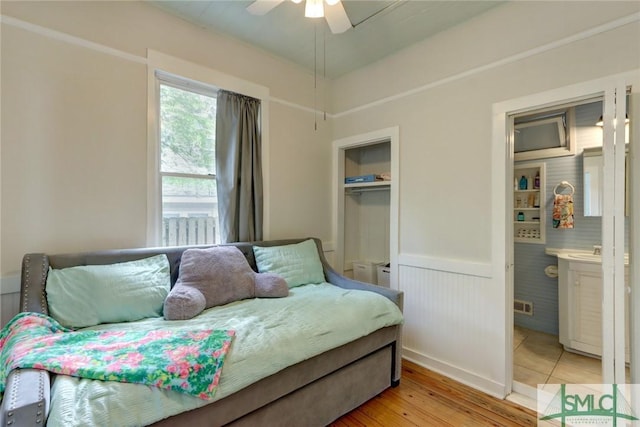 bedroom with a closet, ceiling fan, a wainscoted wall, light wood finished floors, and visible vents