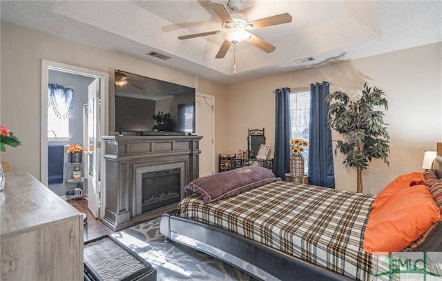 bedroom with a glass covered fireplace, ceiling fan, wood finished floors, and visible vents