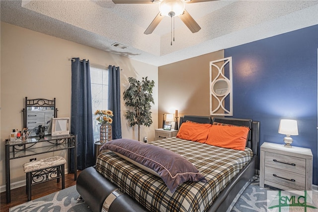 bedroom with ceiling fan, a textured ceiling, visible vents, wood finished floors, and baseboards