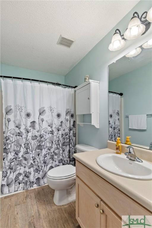 bathroom featuring wood finished floors, vanity, toilet, a shower with shower curtain, and visible vents