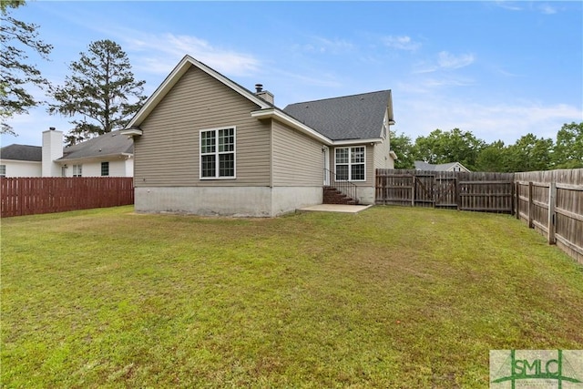 rear view of property with a fenced backyard, a chimney, and a yard