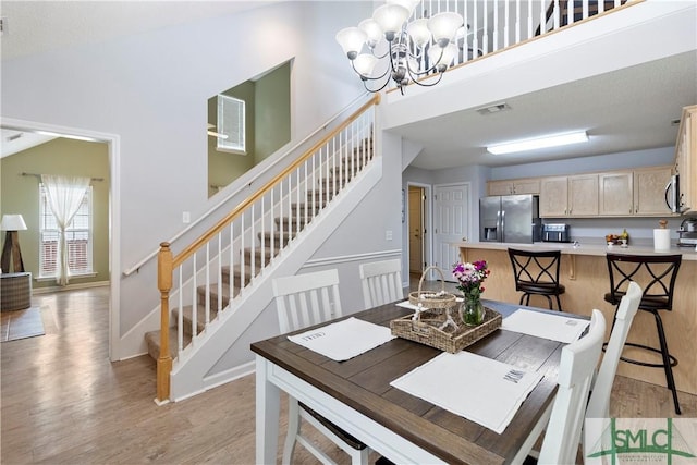 dining area with light wood finished floors, baseboards, visible vents, an inviting chandelier, and stairs