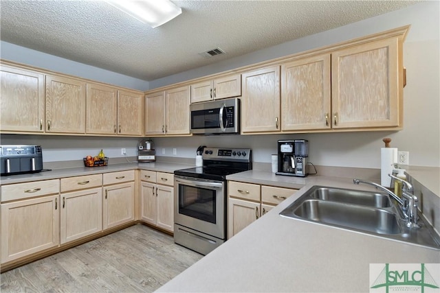 kitchen with light brown cabinetry, stainless steel appliances, visible vents, a sink, and light wood-type flooring