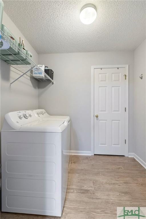 laundry area featuring a textured ceiling, separate washer and dryer, light wood-style flooring, baseboards, and laundry area