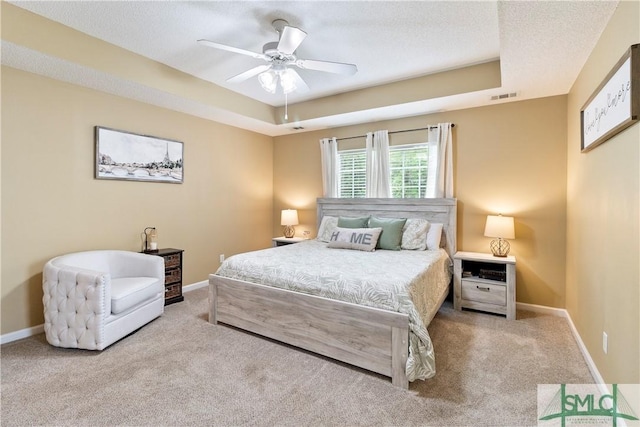 bedroom featuring a tray ceiling, carpet floors, visible vents, and baseboards
