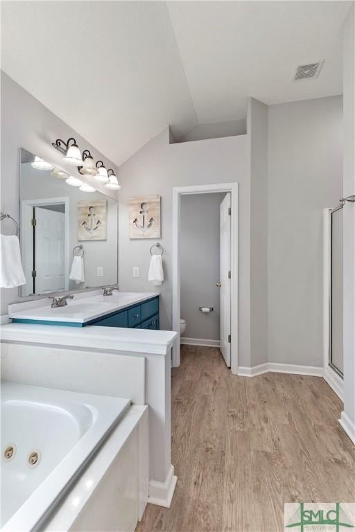full bathroom featuring lofted ceiling, wood finished floors, double vanity, toilet, and a jetted tub