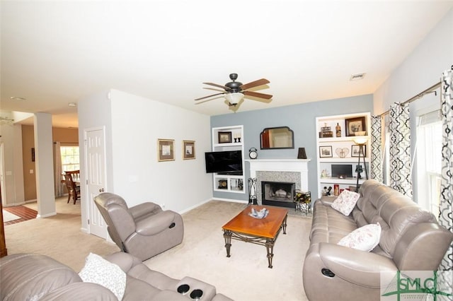 living area with light carpet, baseboards, built in shelves, a ceiling fan, and a fireplace