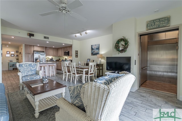living room featuring track lighting, visible vents, a ceiling fan, baseboards, and wood finish floors