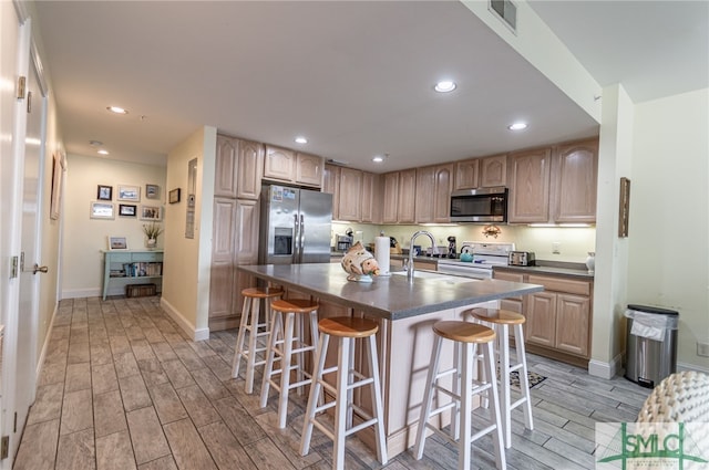 kitchen featuring dark countertops, a kitchen bar, wood finish floors, and appliances with stainless steel finishes
