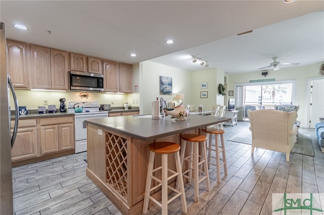 kitchen with wood finish floors, appliances with stainless steel finishes, a breakfast bar, and light brown cabinetry