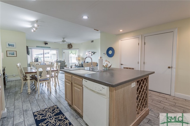 kitchen with light brown cabinetry, dark countertops, dishwasher, a sink, and wood finish floors