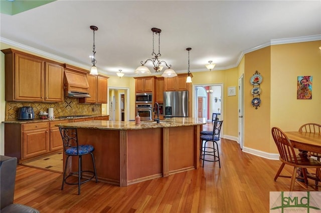 kitchen with light wood-style flooring, decorative backsplash, custom range hood, a breakfast bar, and appliances with stainless steel finishes