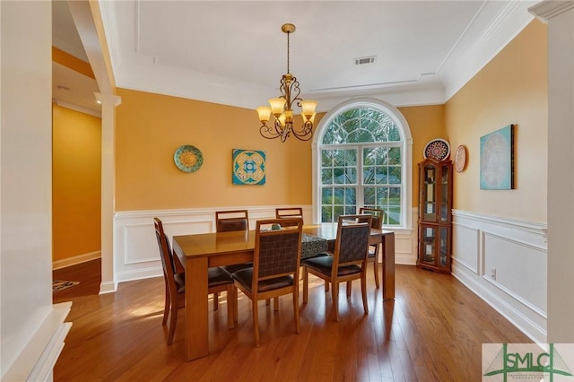 dining area featuring wood finished floors, visible vents, a decorative wall, wainscoting, and a chandelier