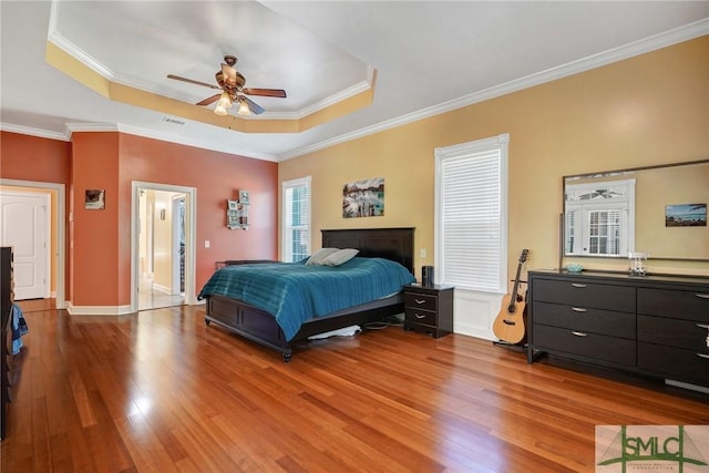bedroom with a tray ceiling, visible vents, a ceiling fan, wood finished floors, and crown molding