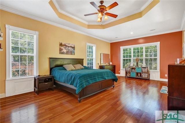 bedroom featuring ornamental molding, multiple windows, wood finished floors, and a raised ceiling