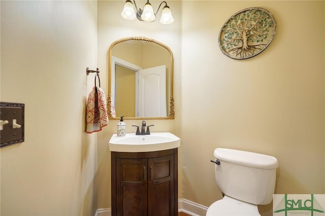 half bath featuring baseboards, toilet, and vanity