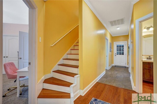 stairway with wood finished floors, visible vents, crown molding, and baseboards