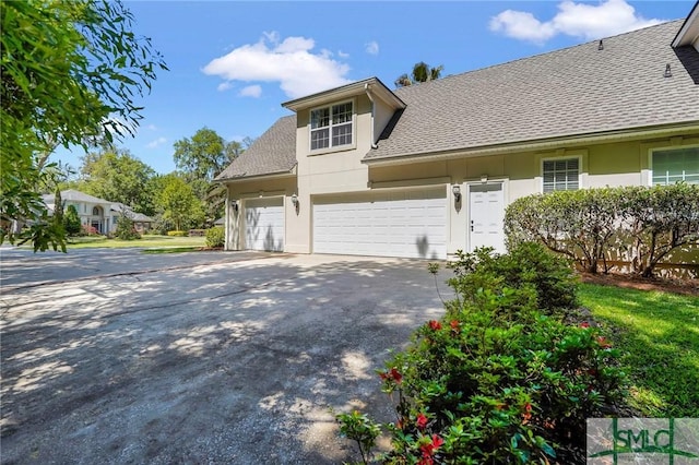 view of side of home with stucco siding, an attached garage, roof with shingles, and concrete driveway