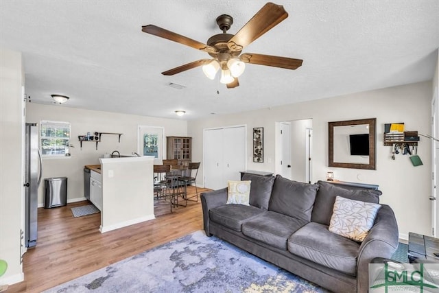 living room with a textured ceiling, baseboards, a ceiling fan, and wood finished floors