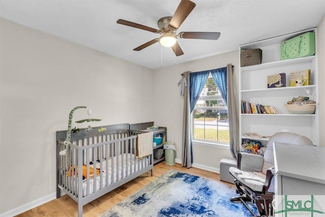 bedroom featuring baseboards, a ceiling fan, a nursery area, and wood finished floors