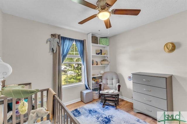 bedroom with a crib, wood finished floors, baseboards, and ceiling fan