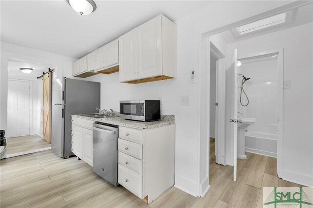 627 W 48th St, Savannah, GA 31405 - kitchen with white cabinets, light wood-style flooring, appliances with stainless steel finishes, and a barn door