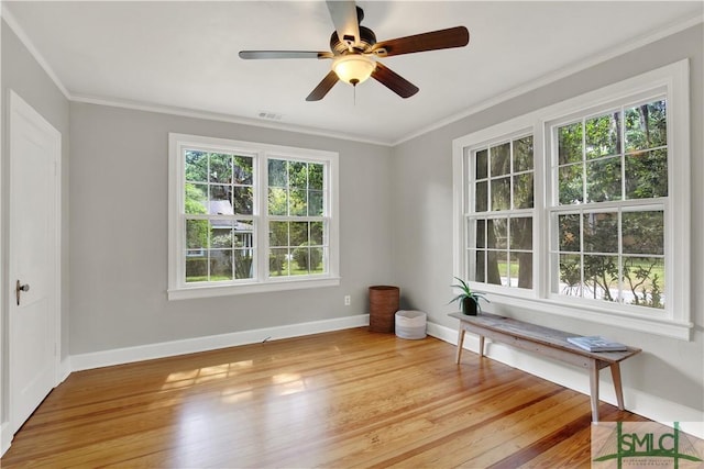 empty room with wood finished floors, ceiling fan, baseboards, visible vents, and crown molding