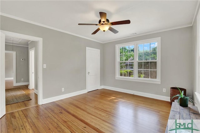 empty room with crown molding, baseboards, attic access, wood finished floors, and a ceiling fan