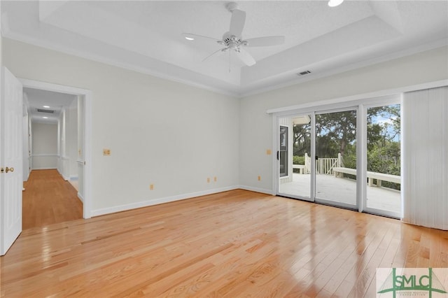 empty room with a ceiling fan, a tray ceiling, visible vents, and light wood-type flooring