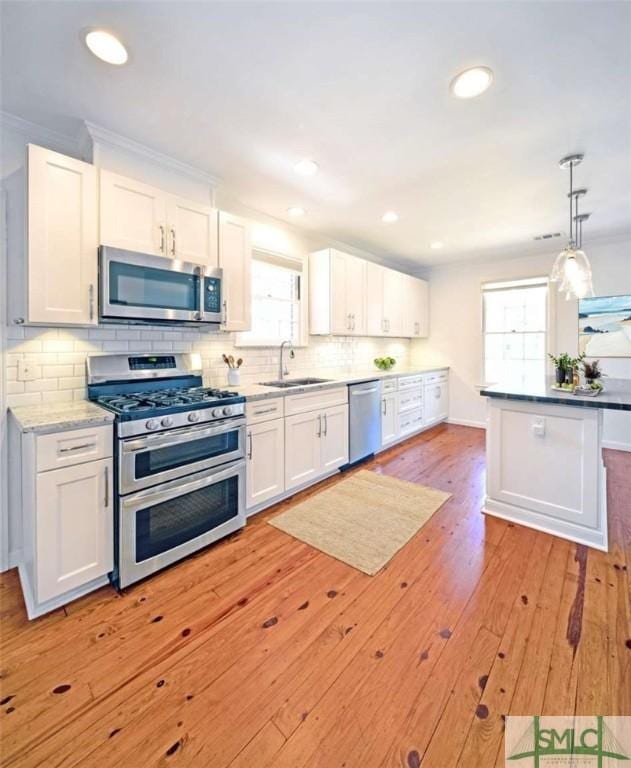 kitchen featuring light wood-style flooring, appliances with stainless steel finishes, white cabinets, backsplash, and a sink
