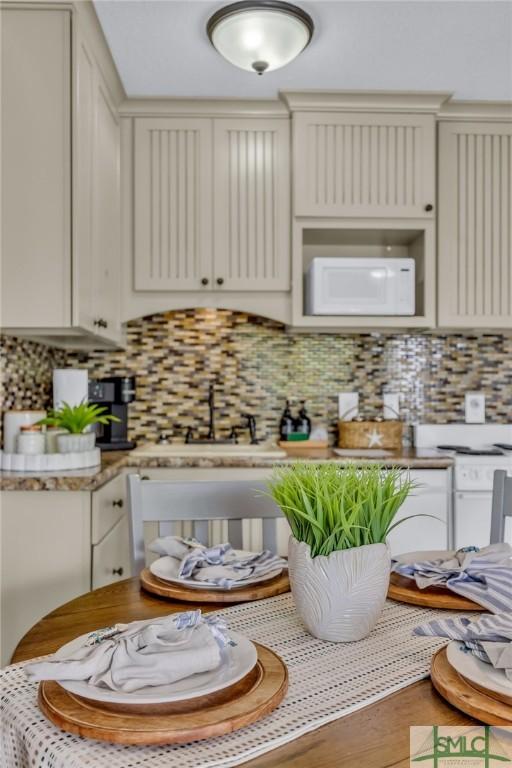1217 Bay St Unit 230A, Tybee Island, GA 31328 - kitchen featuring tasteful backsplash, white microwave, light countertops, a sink, and cream cabinetry
