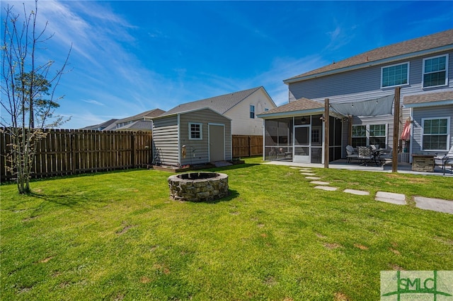 back of property with a sunroom, an outbuilding, a fenced backyard, a storage unit, and a fire pit